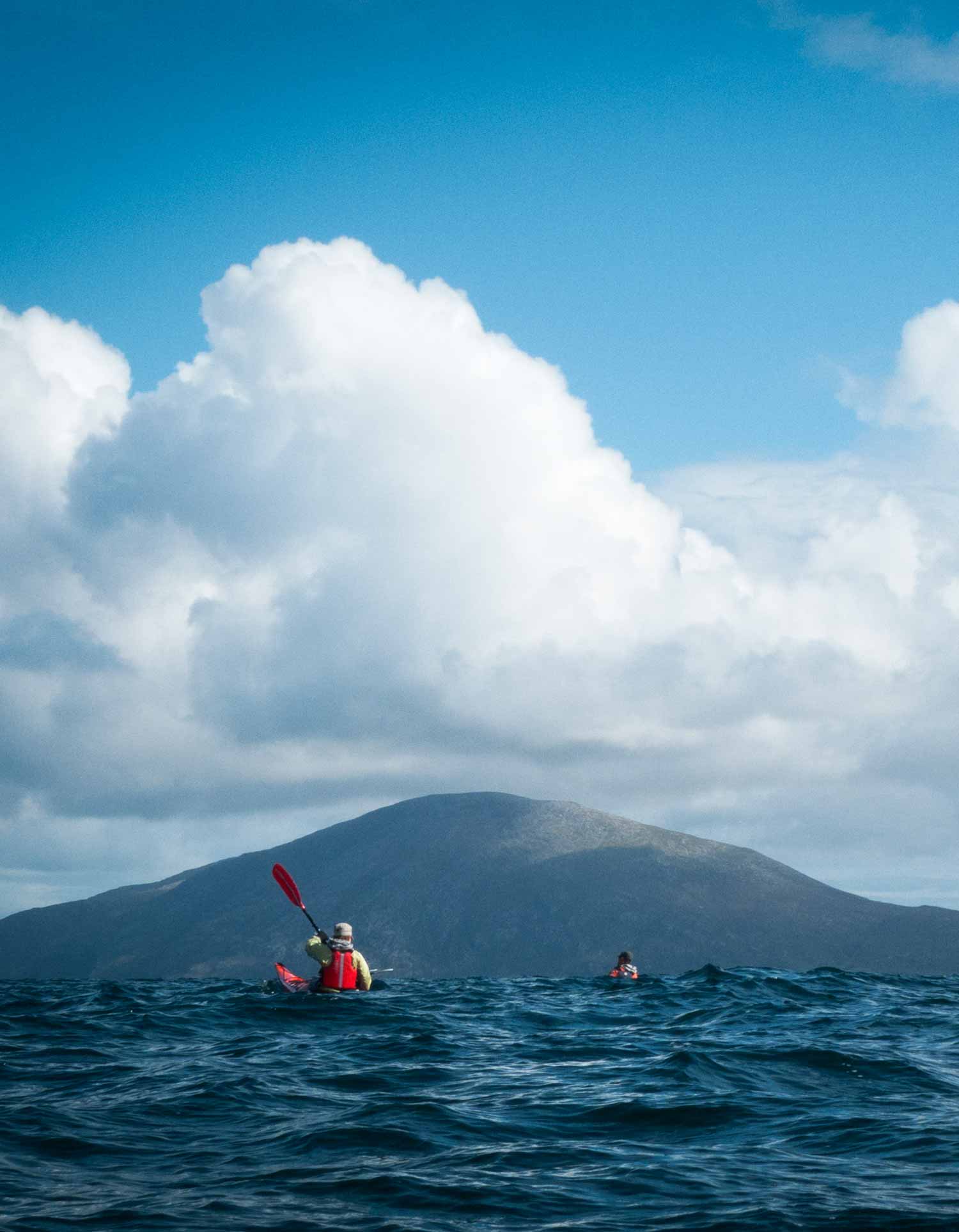 sea kayaks in ocean swells with mountains of Harris 