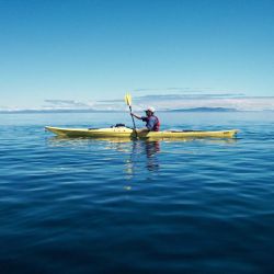 yellow kayak gliding across still, blue ocean